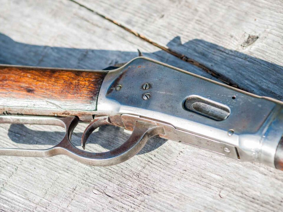 Nahaufnahme eines klassischen Unterhebelrepetierers mit Holzschaft und Metallverschluss, liegend auf verwittertem Holztisch – gut erkennbar ist der charakteristische Unterhebelmechanismus der Waffe.