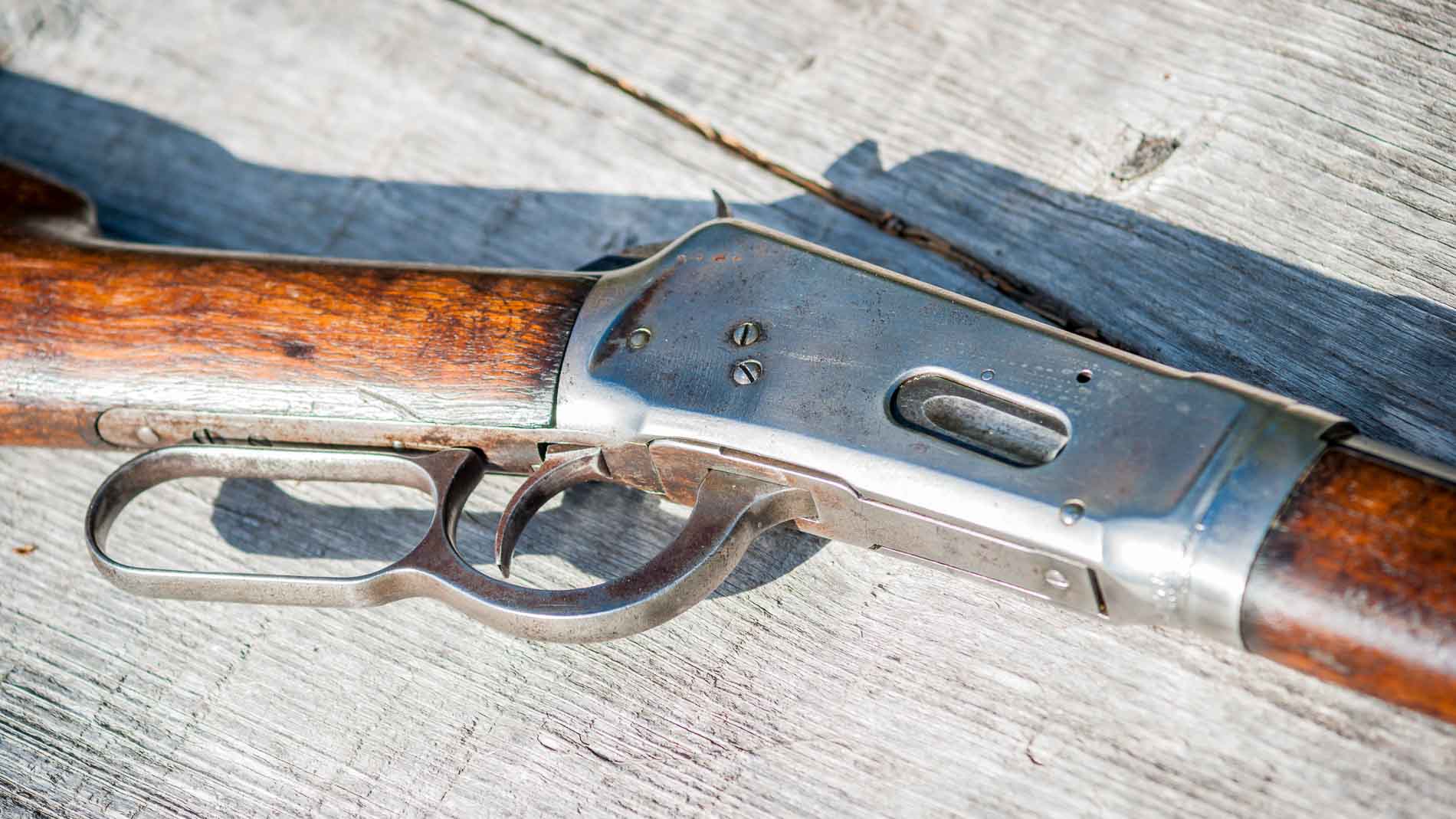 Nahaufnahme eines klassischen Unterhebelrepetierers mit Holzschaft und Metallverschluss, liegend auf verwittertem Holztisch – gut erkennbar ist der charakteristische Unterhebelmechanismus der Waffe.